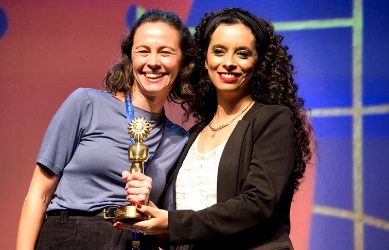 Sofia Ferreira, diretora do IECINE, entrega prêmio a Neli Mombeli, diretora de “Quando a Gente Menina Cresce” - Foto de Capa: Isidoro B. Guggiana